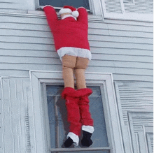 a santa claus decoration is climbing up a window .