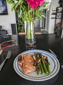 a plate of food with asparagus and mushrooms on a table with a vase of flowers in the background