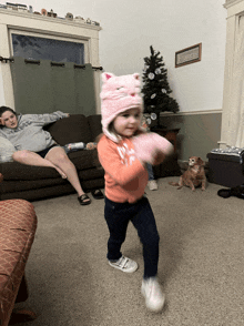 a little girl wearing a pink cat hat and gloves is dancing in a living room