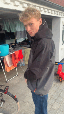 a young man in a black jacket stands in front of a clothesline