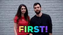 a man and a woman are standing in front of a brick wall with the word first in rainbow letters