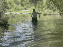 a man in a white tank top and shorts is standing in a river