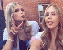 a woman giving a peace sign next to another woman who is sticking out her tongue