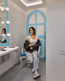 a woman sits on a chair in front of a mirror in a dressing room