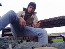 a young man wearing a hat with the letter t on it sits on a wooden bench