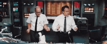 two men in white shirts and ties are dancing in front of a control panel with a clock on it