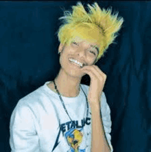 a young man with yellow hair is wearing a metallica shirt and a necklace .