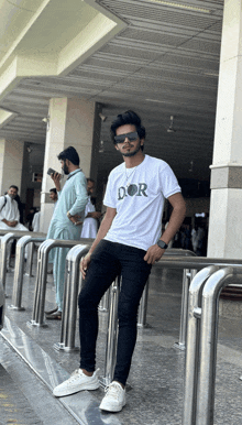 a man wearing a white shirt that says dor is leaning against a railing