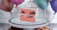 a slice of birthday cake with a face on it and balloons in the background