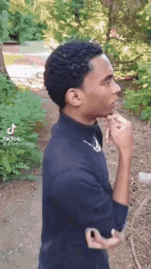 a young man in a black shirt is smoking a cigarette in a park .
