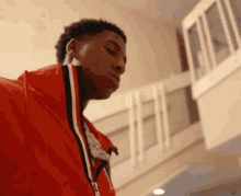 a young man in a red jacket is standing in a room with a balcony .