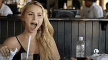 a woman is sitting at a table with her mouth open and a bottle of lifetime water in front of her