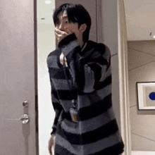 a man in a striped sweater is covering his mouth with his hand while standing in a hallway .