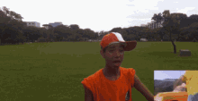 a boy wearing an orange shirt and an orange hat stands in a grassy field with a sign that says south