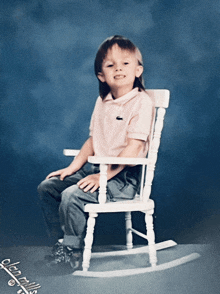 a young boy in a pink shirt is sitting in a white rocking chair with a blue background