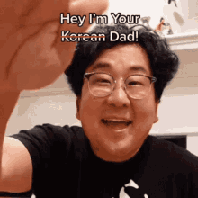 a man wearing glasses and a black shirt is smiling and says hey i 'm your korean dad