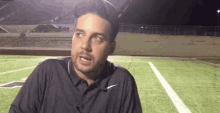 a man in a black nike shirt is standing on a football field talking to someone .