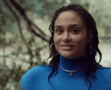 a woman wearing a blue sweater and hoop earrings is smiling and looking at the camera .