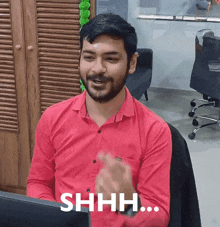 a man in a red shirt is sitting in front of a computer and saying shh