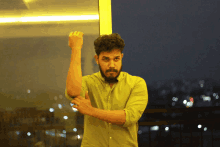 a man in a yellow shirt holds his elbow up in front of a window