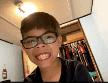 a young boy wearing glasses is making a funny face in front of a closet