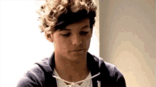 a young man with curly hair is wearing a blue hoodie and a white shirt .