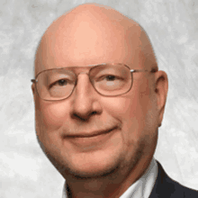 a bald man wearing glasses and a suit smiles at the camera