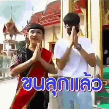 a couple of people standing in front of a building with their hands folded in front of a sign that says ' thailand '