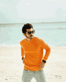 a man wearing sunglasses and an orange sweater is standing on a beach