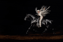 a woman riding a black horse with her arms in the air