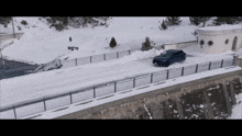 a car is driving on a snowy road next to a stone wall