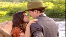 a man in a hat is kissing a woman in a field near a river .