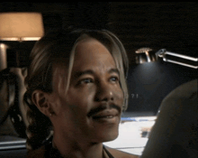 a man with a mustache is smiling in front of a lamp that says ?