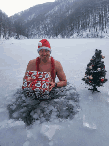 a shirtless man in a santa hat is holding a gift in a frozen lake