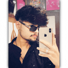 a man wearing sunglasses takes a picture of himself with his iphone