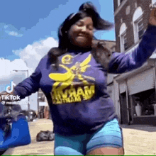 a woman in a purple shirt and blue shorts is dancing in the street .