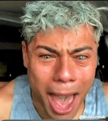 a man with blue hair is crying with his mouth open and his eyes closed .