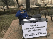 a man sitting at a table with a sign that says change my mind on it