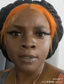 a woman with orange hair is wearing a black hat and a necklace