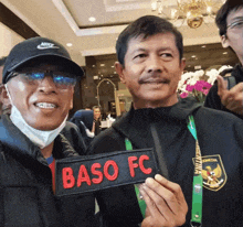 two men are posing for a picture and one has a baso fc patch on his chest