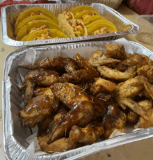 a tray of chicken wings next to a tray of tacos on a table