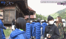 a group of women wearing blue coats are walking in front of a building with chinese writing on the bottom