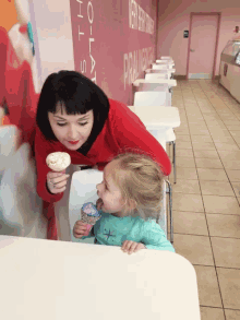 a woman in a red sweater holds an ice cream cone next to a little girl in a green shirt