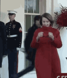 a woman in a red coat is standing in front of a white house with a man in a marine uniform standing behind her .