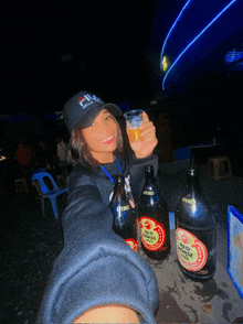 a woman wearing a fila hat holds up a glass of beer