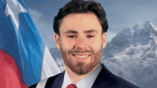 a man in a suit and tie is smiling in front of a flag and mountains .