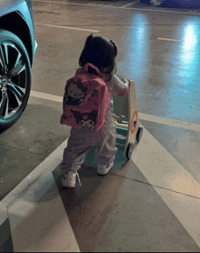 a little girl wearing a pink hello kitty backpack is pushing a walker