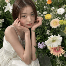 a woman in a white dress is sitting in front of a field of flowers