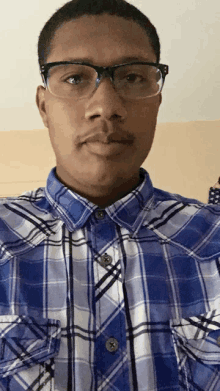 a man wearing glasses and a blue plaid shirt looks at the camera