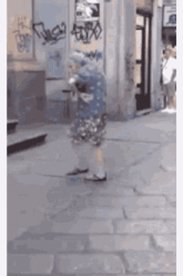an elderly woman is walking down a sidewalk in front of a building .